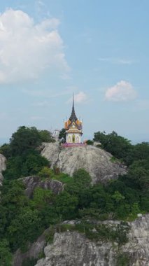 Tayland 'ın ormanlık dağlarındaki büyük bir kayanın üzerinde Budist bir tapınağın etrafında uçan İHA.
