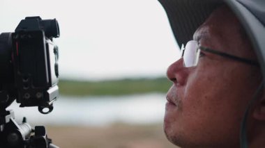 Asyalı fotoğrafçının yüzü ve elleri tripoddaki refleks kamera kontrollerine dokunuyor - 4K Yatay