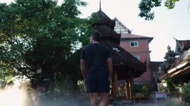 Güneş gözlüğü ve spor ayakkabı takan Latin adam Tayland 'daki Budist tapınağına doğru yavaşça yürüyor. 4K Yatay