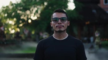 Gözlüklü, gülümsemeden kameraya bakan genç bir Latin adamın yüzünü yakından çek. 4K Yatay