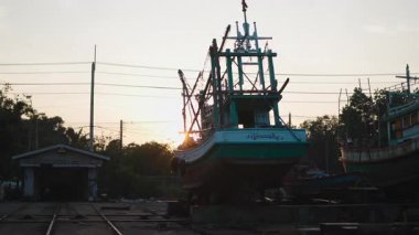 Tahta bir balıkçı teknesi günbatımında bir tersanede blokların üzerinde duruyor - 4K Yatay