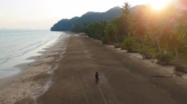Motosikletçi Chumphon, thailand 'daki Aao thung Makham plajı boyunca güzel bir günbatımında manzaranın tadını çıkarıyor - 4k yatay