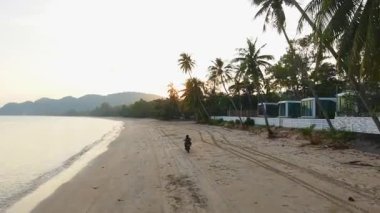 Motosikletçi Chumphon, Tayland 'daki Aao thung Makham plajında güneşin doğuşunu seyrediyor. 4k yatay.