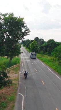 Tayland kırsalındaki verimli bitki örtüsüyle çevrili asfalt bir yolda giden araçlar