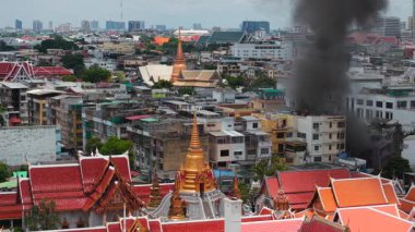 Budist tapınağı yakınlarındaki Bangkoks şehrinde yanan bir binadan koyu duman yükseliyor - 4K Yatay