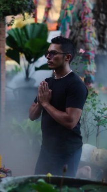 Genç Latin adam, Tayland 'da Buda' nın önünde diz çöküp mum yakıyor. Tam HD Dikey