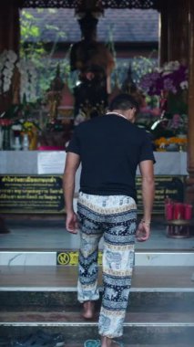 Arkadan gelen Latin çocuk sunağın önünde Buda 'nın yanında dua etmeden önce ayakkabılarını çıkarıyor. Tam HD Dikey
