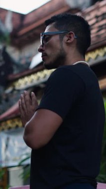 Büyük gözlüklü Latin bir çocuğun Buda 'nın önünde dua ederken yakalanması. Tam HD Dikey