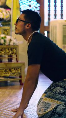 Genç Latin adam Buda 'nın önünde diz çöküp dualarını sunar Altar. Tam HD Dikey