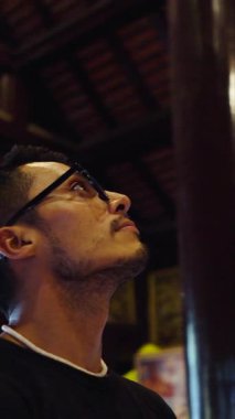 Budist tapınağının güzelliğini sessizce düşünen gözlüklü genç bir Latin 'in yüzüne yakın çekim. Tam HD Dikey