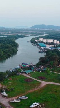 Gün batımında sanayi binaları ve tekneler arasındaki yeşil ormanlardan akan başıboş nehir FullHD Dikey