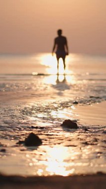 Gün batımında denizde yürüyen ve el sallayan genç bir adam arkasında günbatımı olan FullHD Dikey