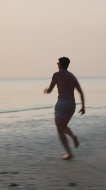 Gün batımında sığ sularda koşan ve eğlenen genç adam FullHD Dikey