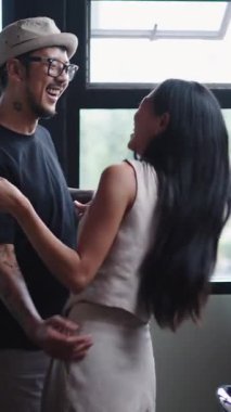 Genç Asyalı çift mutfakta dans edip eğlenirken kahvenin tadını çıkarıyor.