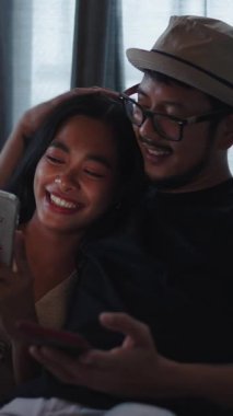 Mutlu genç Asyalı çift, rahatlarken ve diziyi izlerken akıllı telefonlar kullanıyor.