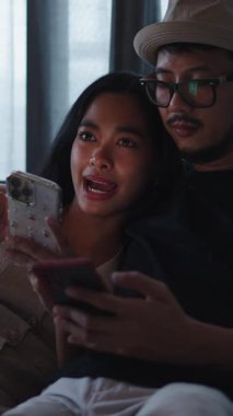 Akıllı telefonlarıyla sosyal medyaya bakan Asyalı mutlu genç çift - FullHD dikey