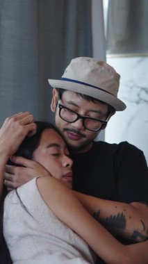 Genç Asyalı romantik çift evlerindeki kanepede birbirine sokulmuş dövmeli FullHD dikey