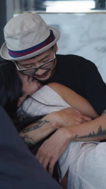 Asyalı erkek ve kız rahat bir kanepede sarılıp sevgi gösteriyorlar.