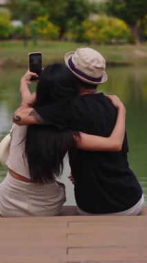 Romantik çift gölün kıyısında, FullHD dikey, huzurlu bir anın tadını çıkarırken selfie çekiyor.