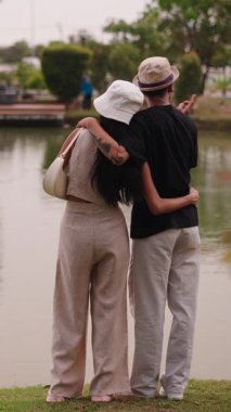 Şehir parkındaki göl kıyısında ayakta duran romantik çift FullHD Dikey