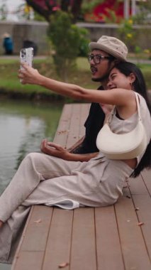 Genç Taylandlı çift gölün kenarında selfie çekiyor ve eğleniyorlar.