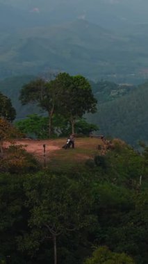 Ormanlarla dolu bir dağın tepesindeki yalnız motorcu ve insansız hava aracı manzaralı bir bitki örtüsü.