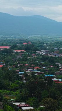 Sessiz bir köy, bulutların altındaki bir dağ silsilesiyle çevrili yemyeşil bir vadinin ortasında, FullHD dikey