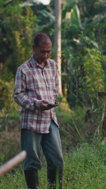 Ormanda yeşil bir alanda duran bir tarım işçisi akıllı telefonu sakince manipüle ediyor.