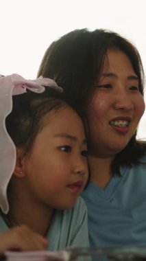 Evde FullHD dikey dizüstü bilgisayarda videolar izleyip gülen mutlu Asyalı anne ve kız.