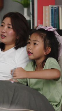 Asyalı anne ve kızı büyük bir kanepede çıplak ayakla film izlemekten zevk alıyorlar.