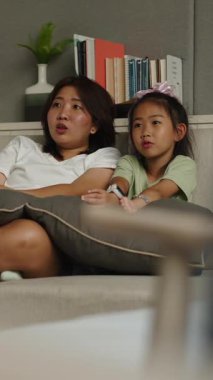 Anne ve kızı, rahat oturma odalarında, FullHD dikey bir şekilde televizyon izleyerek rahatlıyor.