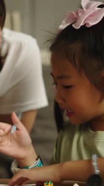 Asyalı bir anne, genç kızına evde FullHD dikey bir defter yazıp öğrenmesine yardım eder.