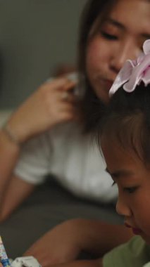 Genç Asyalı anne evde kızına yazma alıştırmasında yardım ediyor.