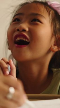 Mutlu Asyalı kız annesinin yardımıyla bir deftere yazıp çiziyor, FullHD Dikey