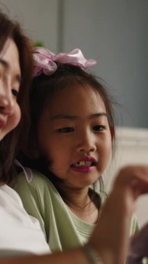 Asyalı anne ve kızı evde boş zamanlarının tadını çıkarırken akıllı telefon kullanıyorlar.