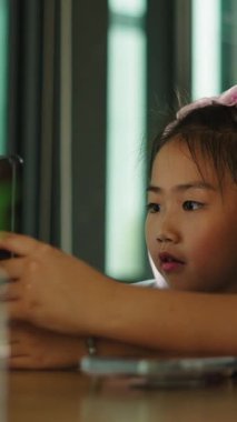 Bir anne, genç kızına oturma odasındaki masada otururken tablet kullanmasında yardım eder.