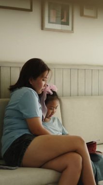 Genç bir Asyalı anne kızıyla birlikte oturma odasındaki kanepede tablet kullanırken - FullHD Dikey