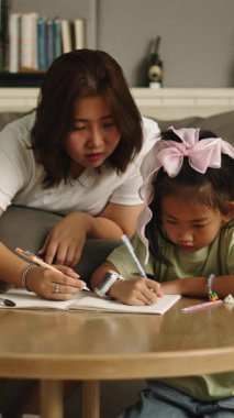 Annem küçük kızına oturma odasındaki kahve masasında oturup yazı yazmayı ve resim çizmeyi öğretiyor.