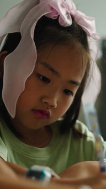 Kafasında yay olan Asyalı bir kız öğretmeninin yardımıyla yazmayı öğreniyor.