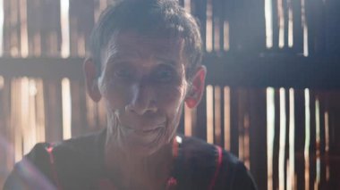 Güneş ışığı, bambu kulübesinde poz veren yaşlı bir Asyalı kadının yüzünü aydınlatıyor - 4K Yatay