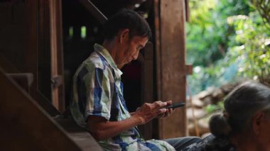 Lahu kabilesinin kıdemli adamı geleneksel verandada cep telefonu kullanıyor - 4K Yatay