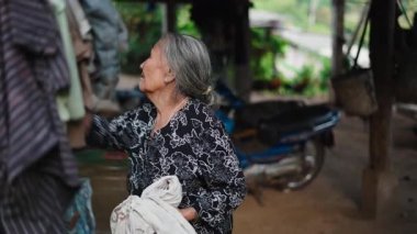 Yaşlı Güneydoğu Asyalı Kadın Çamaşır ipinde Kuruyacak Elbiseler Asıyor - 4K Yatay