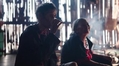 Yaşlı bir Asyalı kadın, loş bir lahu evinde karısıyla bir bardak çayın tadını çıkarıyor - 4K Yatay