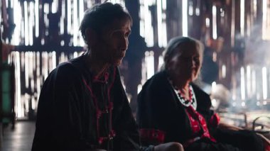 Geleneksel kıyafetler giymiş yaşlı bir Asyalı ahşap bir kulübede çay içiyor - 4K Yatay