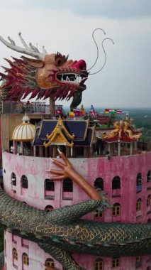 Ejderha heykeli Tayland 'daki Wat Samphran tapınağında canlı pembe bir kule etrafında kıvrılır.