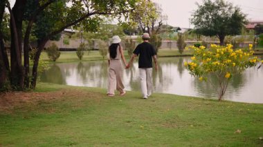 Romantik çift, resim parkında göletin kenarında sessiz bir yürüyüş yapıyor. 4K Yatay.
