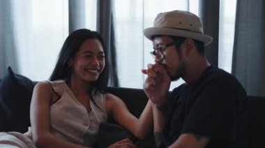 Kanepede el ele tutuşup kahkahalar atan mutlu Asyalı çift - 4K Yatay