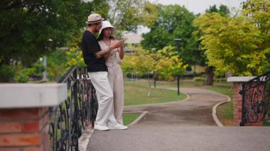 Şehir parkında telefon üzerinden komik sosyal medya içeriğini paylaşan turist çifti - 4K Yatay