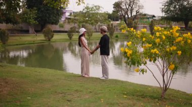 Romantik Asyalı genç çift Şehir Parkı Gölü 'nün kenarında çimde sohbet ediyorlar - 4K Yatay