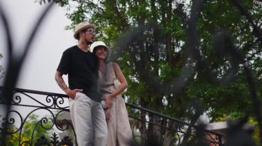 Genç Taylandlı çift parkta romantik bir anın tadını çıkarıyor. Korkuluklara yaslanıyor ve gülümsüyor - 4K Yatay